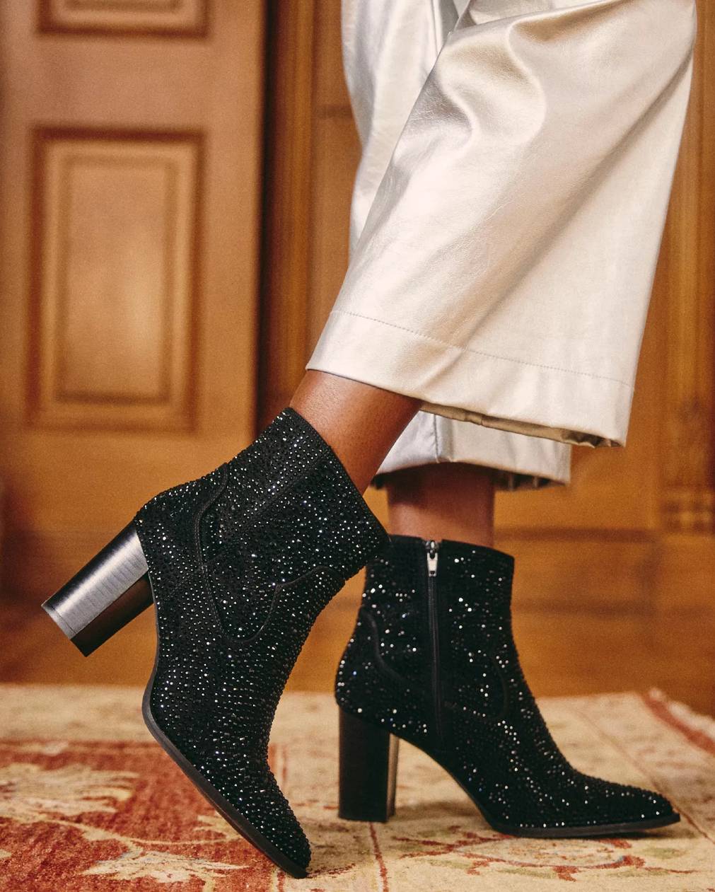A person wears a pair of black sparkly ankle boots