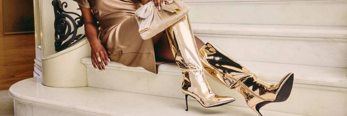 A woman wears a festive gold dress with thigh high gold boots