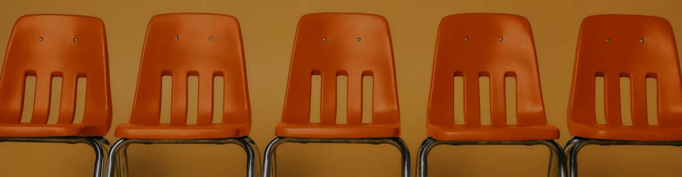 Five orange school chairs in a row.
